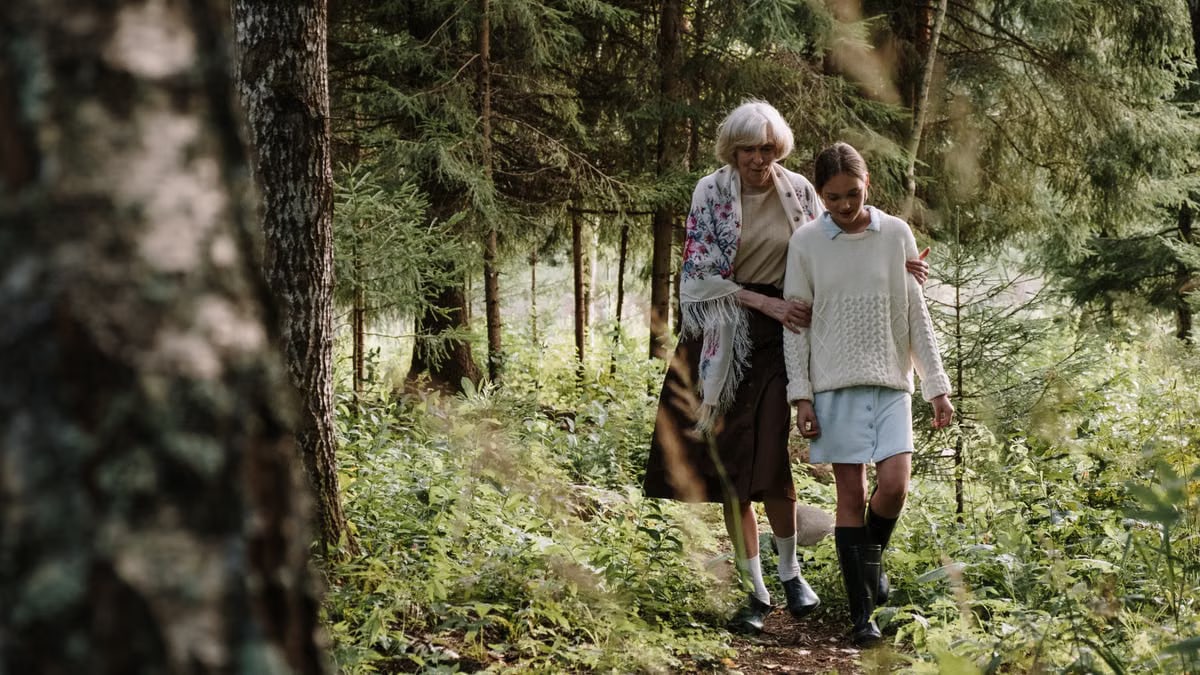 A loving moment between a grandmother and granddaughter walking through a tranquil forest path.
